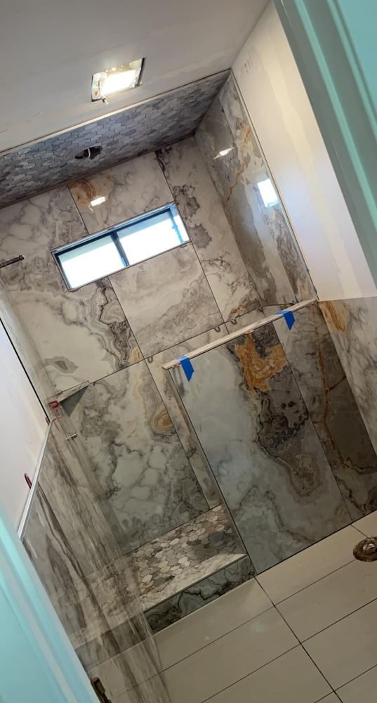 Freshly tiled walk-in shower with marble-look walls and a glass panel